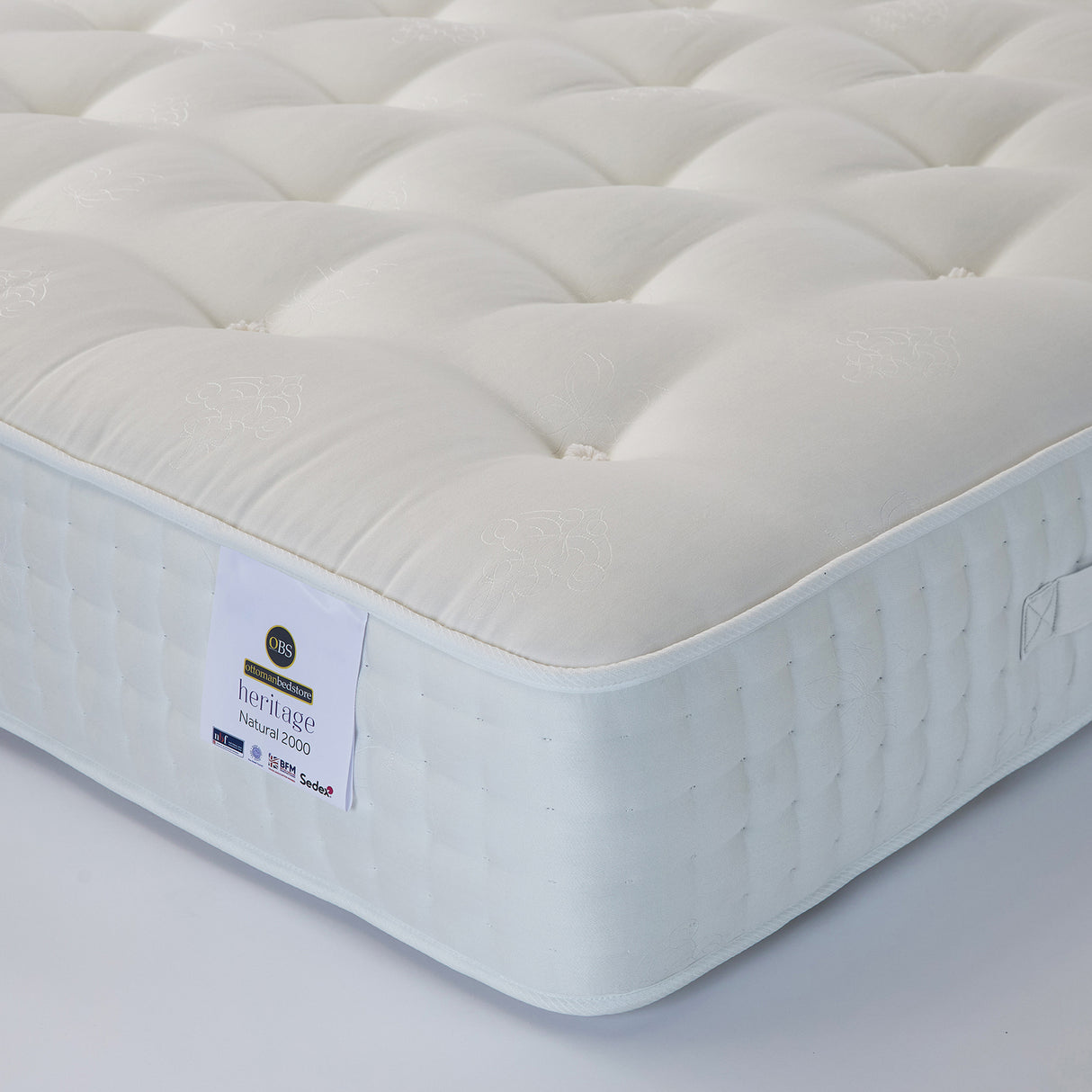 A white, pocket sprung mattress with visible tufting and a label indicating the brand 'Ottoman Bed Store' and the model ' Heritage Natural 2000'.
